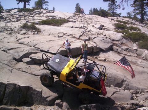1989 Ford Bronco - An off-road vehicle with a roll cage and an American flag navigates a challenging rocky landscape.