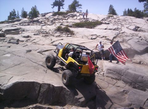 1989 Ford Bronco - A yellow open-top tube-frame rock buggy on oversized mud-terrain tires climbs bare granite slabs on a mountain trail, driver strapped in be…