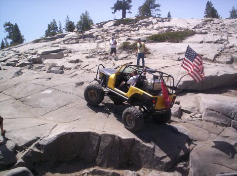 1989 Ford Bronco - A modified off-road vehicle tackles a challenging rocky trail under a clear blue sky.