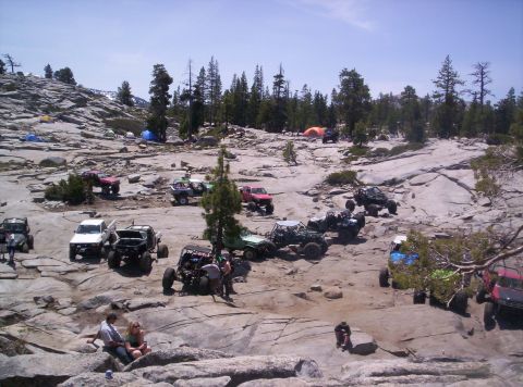 1989 Ford Bronco - Multiple off-road vehicles are gathered on a rocky landscape with tents set up in the distance.