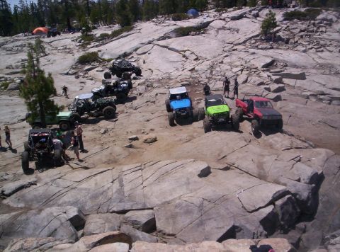 1989 Ford Bronco - A group of modified off-road vehicles are gathered on a rocky, uneven terrain, suggesting an outdoor adventure or trail event.