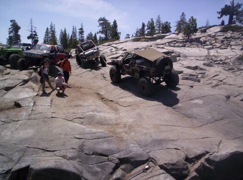 1989 Ford Bronco - Several off-road vehicles navigate a challenging rocky landscape under a clear blue sky.