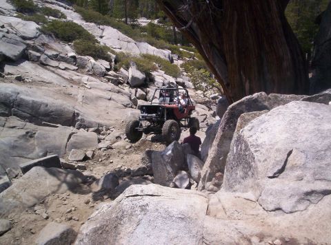 1989 Ford Bronco - A red off-road buggy tackles a challenging rocky incline on a sunny day.