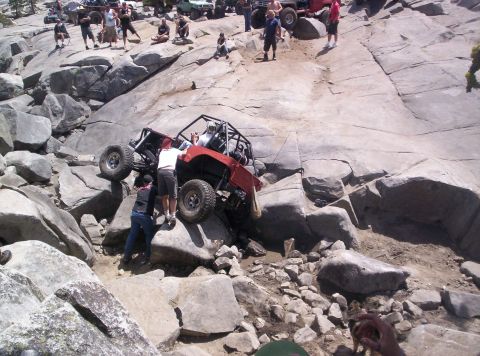 1989 Ford Bronco - A group of people watch as a modified off-road vehicle attempts to climb a challenging rocky terrain.