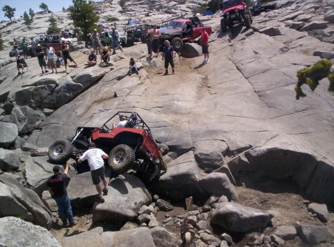 1989 Ford Bronco - Multiple off-road vehicles are shown navigating a challenging rocky incline, with people observing the action.