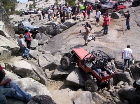 1989 Ford Bronco - Off-road enthusiasts tackle a challenging rocky course, with multiple vehicles and onlookers present.
