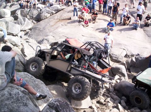 1989 Ford Bronco - A custom-built off-road buggy attempts to traverse a challenging rocky obstacle course with spectators watching.