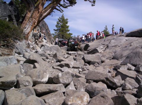 1989 Ford Bronco - Several off-road vehicles are navigating a challenging rocky trail, with a crowd of people observing the action.