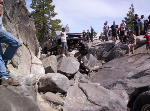 1989 Ford Bronco - A modified off-road vehicle attempts to traverse a difficult rocky terrain while onlookers observe the action.