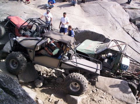 1989 Ford Bronco - Multiple custom off-road vehicles are attempting to traverse a challenging rocky incline, with people observing the action.