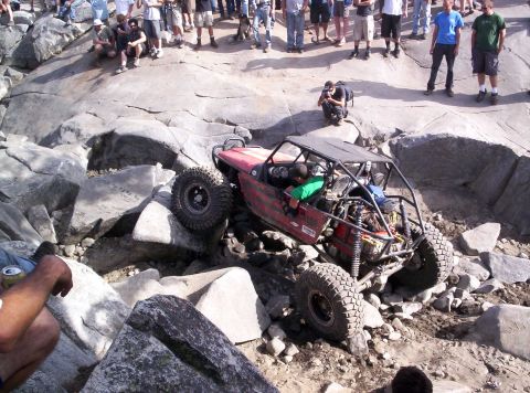 1989 Ford Bronco - A heavily modified off-road buggy attempts to traverse a rocky terrain with spectators watching.