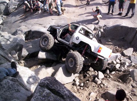 1989 Ford Bronco - A modified off-road truck is shown attempting to climb over large rocks on a challenging trail.