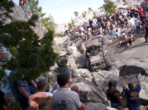 1989 Ford Bronco - A crowd watches an off-road vehicle attempt to traverse a difficult rocky terrain.