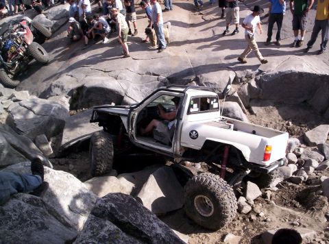 1989 Ford Bronco - A modified pickup truck navigates a challenging rocky obstacle course with spectators watching.