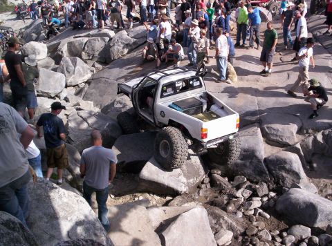 1989 Ford Bronco - Off-road truck attempts to climb over large rocks with spectators observing the action.