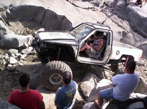 1989 Ford Bronco - A modified pickup truck is attempting to climb over large rocks on a trail, with onlookers observing the action.