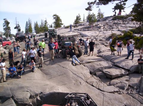 1989 Ford Bronco - A group of people and several off-road vehicles are on a rocky, uneven terrain under a clear sky.