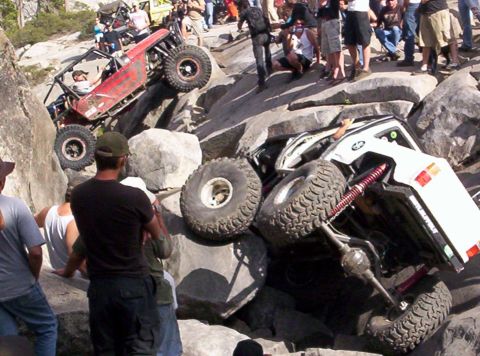1989 Ford Bronco - Two off-road vehicles tackle a challenging rocky course, with spectators watching the action.
