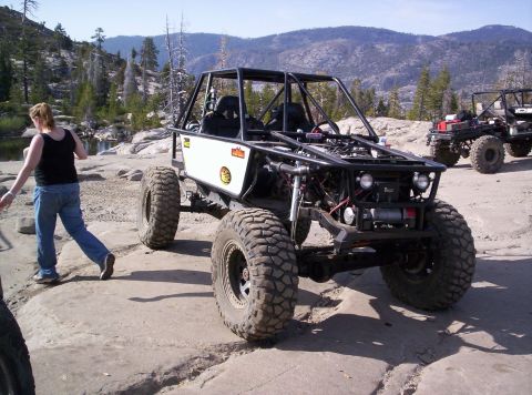 1989 Ford Bronco - Two custom off-road vehicles are parked on a rocky landscape with mountains in the distance.