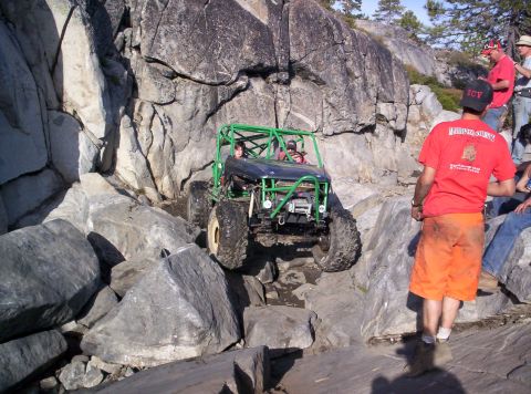 1989 Ford Bronco - An off-road buggy with a prominent green roll cage tackles a challenging rocky obstacle.