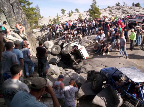 1989 Ford Bronco - Spectators watch as off-road vehicles navigate a challenging rocky course, with one vehicle overturned.