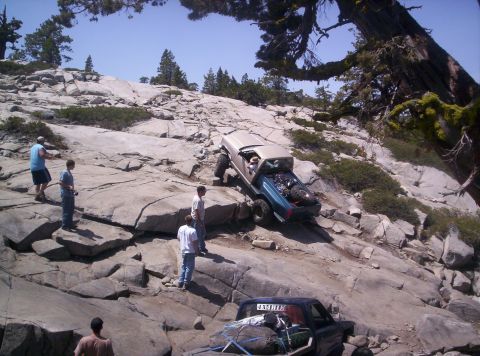 1989 Ford Bronco - Off-road enthusiasts tackle a challenging rocky trail under a clear blue sky.