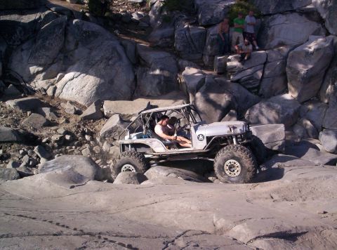 1989 Ford Bronco - A custom off-road buggy navigates a rocky trail with spectators observing from above.