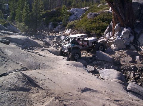 1989 Ford Bronco - A custom off-road vehicle tackles a steep, rocky incline in a mountainous area.