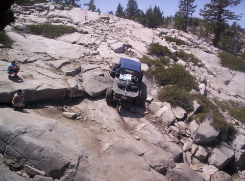 1989 Ford Bronco - An off-road vehicle tackles a challenging rocky incline with spectators observing the difficult maneuver.