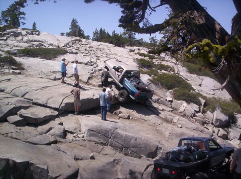1989 Ford Bronco - Off-road vehicles tackle a challenging rocky trail under a clear blue sky.