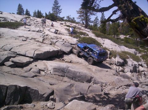 1989 Ford Bronco - A blue SUV navigates a challenging rocky terrain on a sunny day.