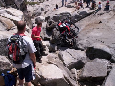 1989 Ford Bronco - An off-road buggy navigates a difficult rocky terrain, with spectators observing the challenging maneuver.