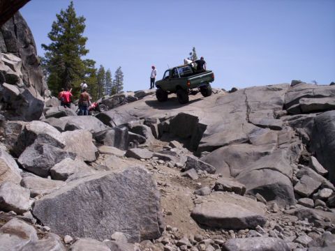 1989 Ford Bronco - A group of people watch as a modified green pickup truck navigates a challenging rocky terrain.