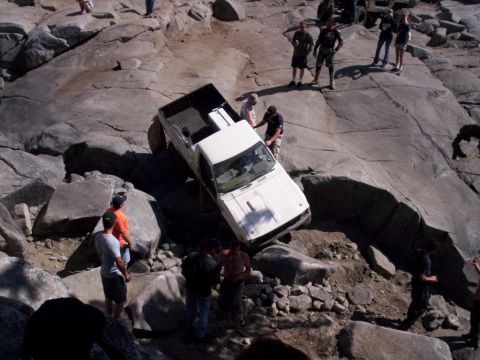 1989 Ford Bronco - White pickup truck attempts to drive over a challenging rocky obstacle course.