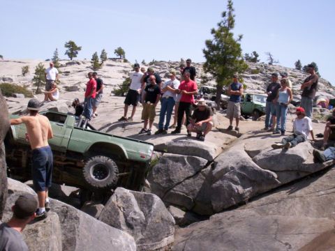 1989 Ford Bronco - A group of people watch as a modified pickup truck navigates a challenging rocky terrain.