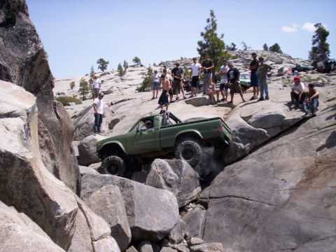 1989 Ford Bronco - A group of people watch a green pickup truck off-road through a rocky terrain.