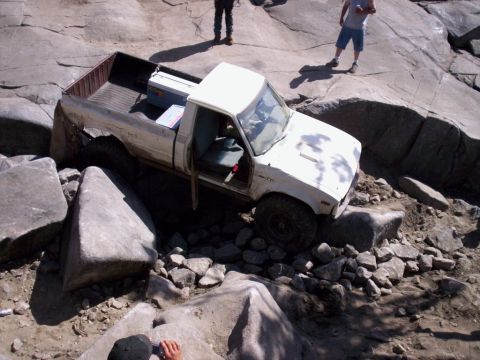 1989 Ford Bronco - White pickup truck is shown off-roading over large rocks and boulders.