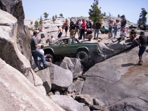 1989 Ford Bronco - A green pickup truck is shown off-roading over large rocks with a crowd watching.