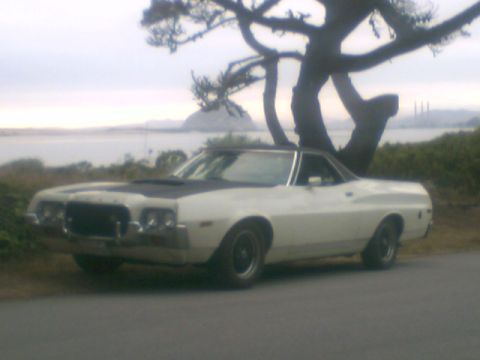 1972 Ford Ranchero - White 1972 Ford Ranchero with a black hood accent sits by a tree with a coastal background.
