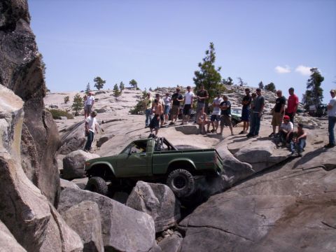 1989 Ford Bronco - A group of people watch as a modified pickup truck navigates a challenging rocky terrain.
