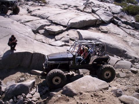 1989 Ford Bronco - A modified off-road jeep with a prominent roll cage is seen traversing a challenging rocky landscape, with another vehicle visible in the b…