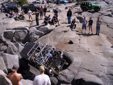 1989 Ford Bronco - A heavily modified off-road vehicle navigates a challenging rocky terrain with spectators watching.