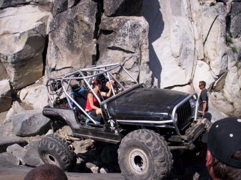 1989 Ford Bronco - A heavily modified Jeep Wrangler navigates a rocky off-road trail with passengers inside.
