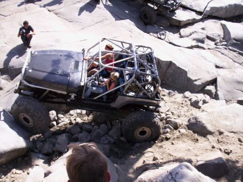 1989 Ford Bronco - A heavily modified off-road vehicle with a roll cage is being driven over large rocks on a trail.