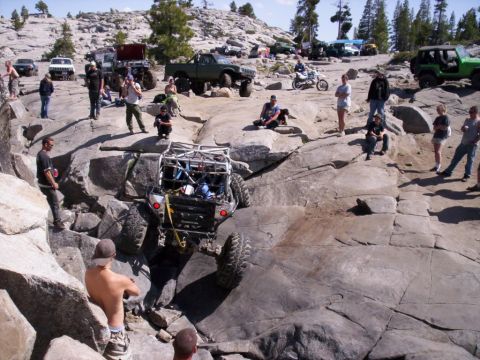 1989 Ford Bronco - A custom off-road buggy navigates a rocky terrain with spectators watching.