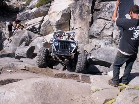 1989 Ford Bronco - A modified off-road vehicle tackles a challenging rocky trail with a person watching.