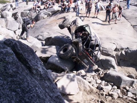 1989 Ford Bronco - An off-road vehicle is overturned on a rocky terrain, with a crowd of people observing the scene.