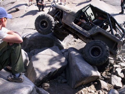 1989 Ford Bronco - A heavily modified off-road vehicle attempts to traverse a rocky terrain with a spectator watching.