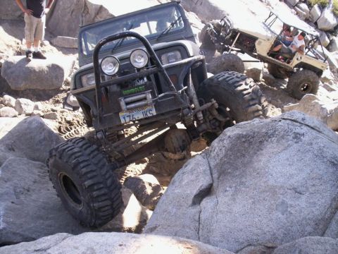 1989 Ford Bronco - Two off-road vehicles tackle a challenging rocky trail under a bright sun.