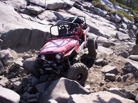 1989 Ford Bronco - A red off-road jeep is shown traversing a challenging rocky landscape.